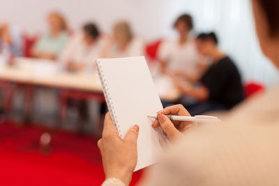 Cropped image of woman writing on spiral notebook during seminar