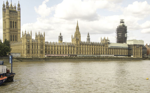 View of buildings by river against cloudy sky