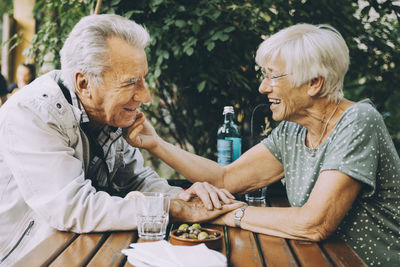 Smiling senior woman touching partner's cheek while sitting at restaurant in city