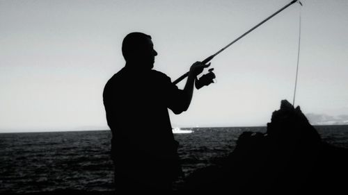 Silhouette man fishing at sea against clear sky