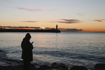 Rear view of silhouette woman standing by sea against sky during sunset