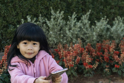 Portrait of cute girl holding mobile phone by plants