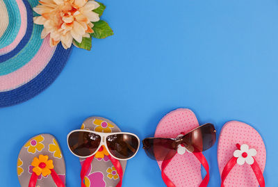 High angle view of sunglasses with flip-flops on blue background