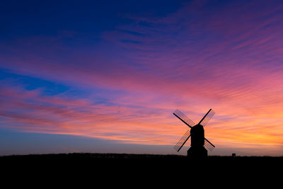 Silhouette traditional windmill on field against sky during sunset