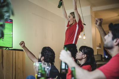 Excited fans cheering for team while watching soccer match in living room