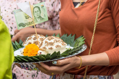 Midsection of woman holding religious offerings with paper currency