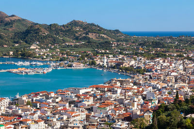 Aerial view of townscape by sea against blue sky