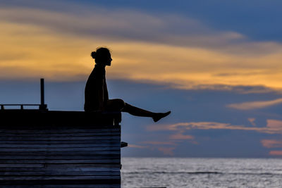 Silhouette woman sitting over sea against sky during sunset