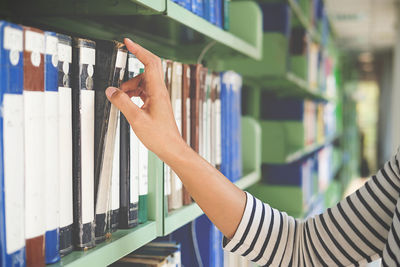 Cropped hand of woman removing book from bookshelf in library