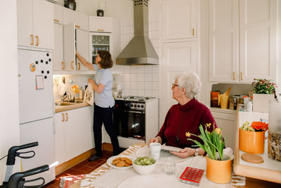 Senior woman looking at female healthcare worker working in kitchen