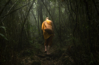 Rear view of monk wearing traditional clothing walking in forest