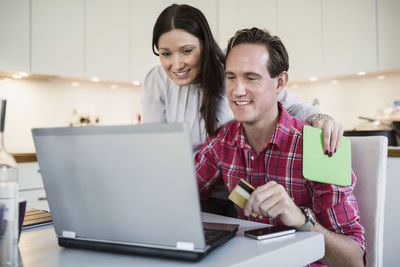 Smiling couple shopping online through credit card and laptop at home
