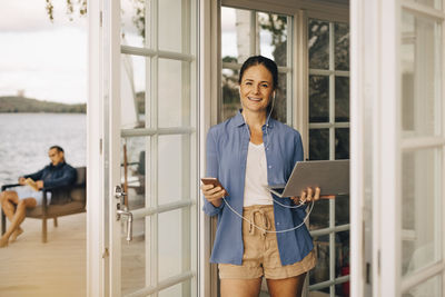 Portrait of mature woman using mobile phone and laptop with man in background