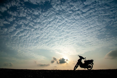 Silhouette man riding bicycle against sky during sunset