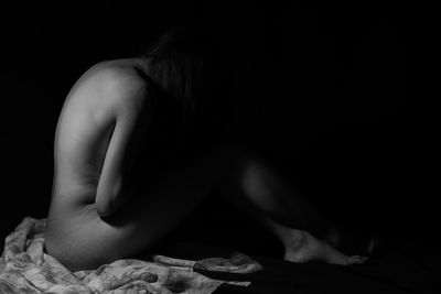 Side view of naked woman sitting in darkroom