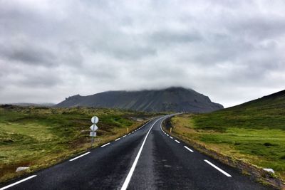 Road passing through mountain against cloudy sky