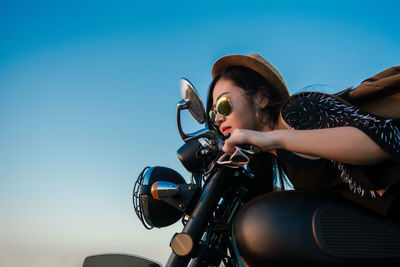 Young woman sitting on motorcycle at road against sky