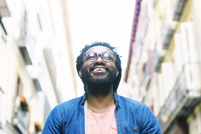 Low angle view of smiling young man wearing eyeglasses looking away in city