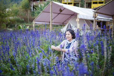 Smiling woman amidst purple flowering plants on field