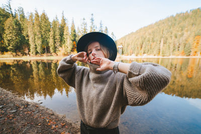 Woman standing by lake against trees