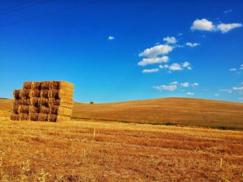 Hay bales on field against blue sky