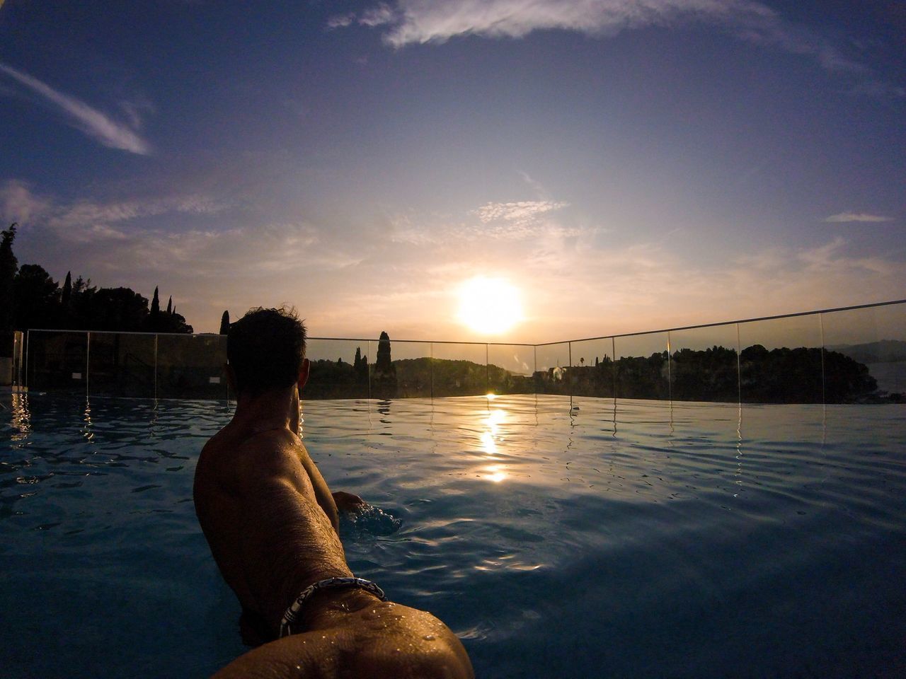 MAN AT SWIMMING POOL AGAINST SKY DURING SUNSET