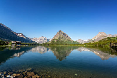 Scenic view of lake by mountains against clear blue sky