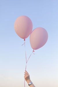 Low angle view of woman holding pink helium balloons against sky