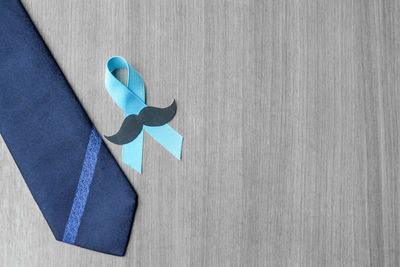 Directly above view of blue ribbon with mustache by necktie on table