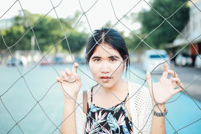 Portrait of young woman standing by chainlink fence