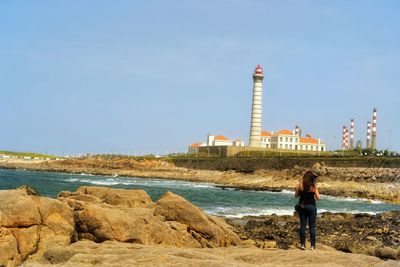 Rear view of woman standing on rocky sea shore against sky