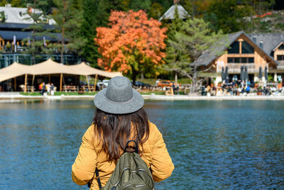 Rear view of woman standing on shore of lake, looking at beautiful tourist resort