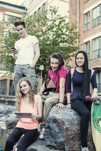 Portrait of smiling high school students sitting on rock at schoolyard