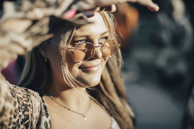 Close-up of smiling woman sheilding eyes while looking away in summer