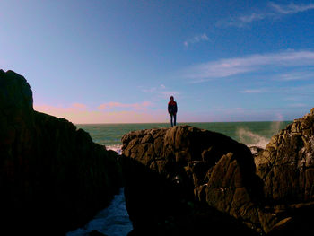 Man standing on rock by sea against sky