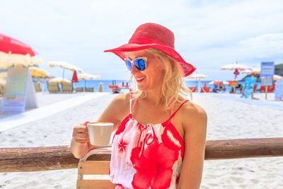 Close-up of woman holding coffee cup standing at beach