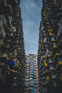 Low angle view of man photographing residential buildings against sky