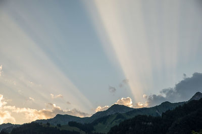 Sunlight streaming through mountain range against sky