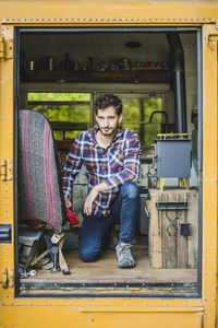 Full length portrait of confident young man kneeling in motor home