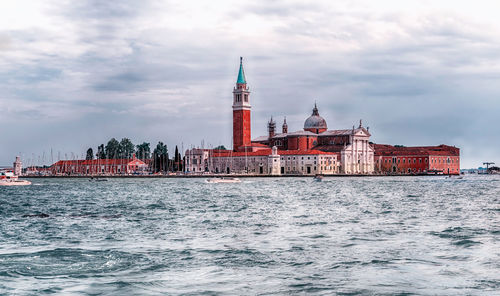 View of buildings by sea against cloudy sky