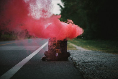 Smoke emitting from umbrella held by man sitting on road