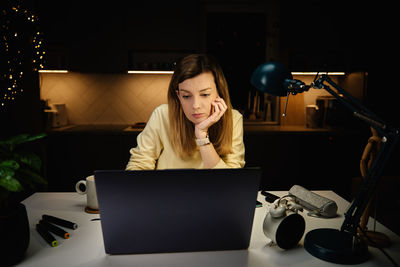 Woman works at home office at night, using laptop