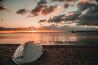 Upside down boat moored on shore at beach against sky during sunset