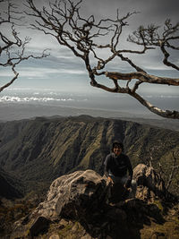 Man sitting on rock against sky