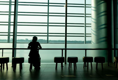 Rear view of silhouette girl sitting by window at airport