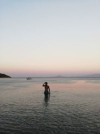 Man in sea against clear sky during sunset