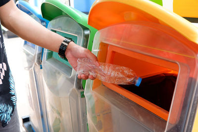 Cropped hand of man putting plastic bottle in garbage bin