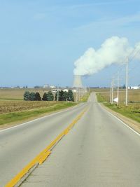 Road leading towards factory against sky