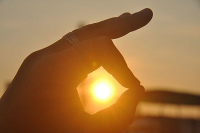 Close-up of hand holding sun during sunset