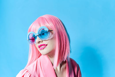 Portrait of young woman wearing sunglasses against blue background